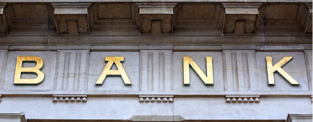 Gold letters spelling "BANK" on a classical stone building facade.