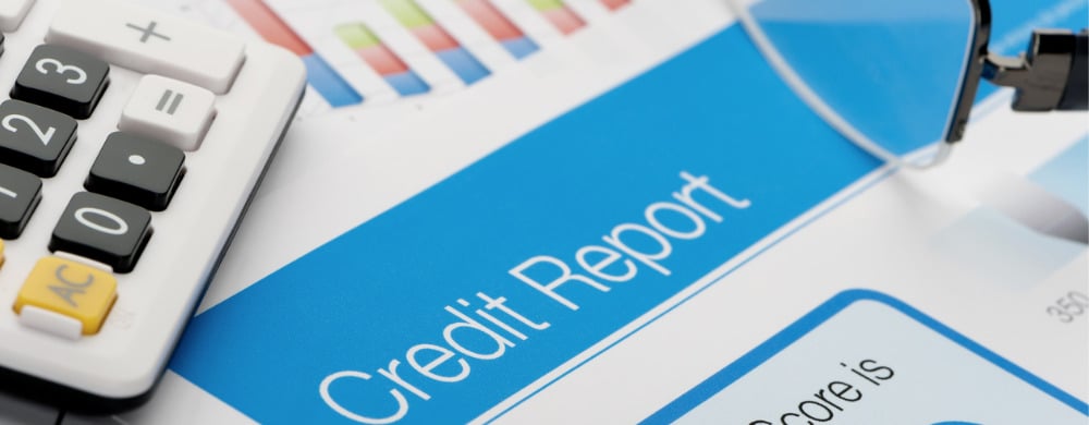 A calculator and credit report document displayed on a desk with financial charts.