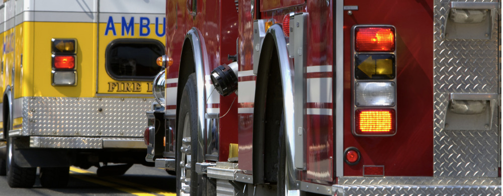 Yellow ambulance and red fire truck parked side by side showing their rear sections.