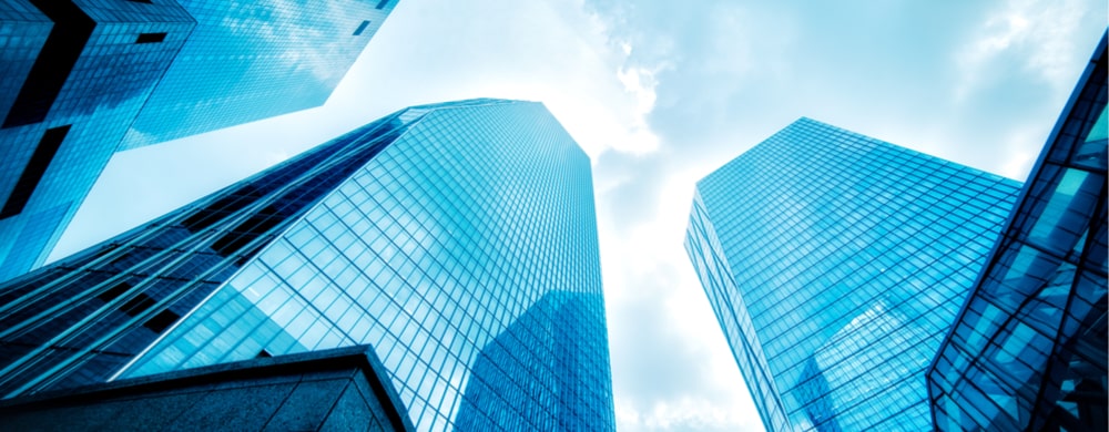 Upward view of modern glass skyscrapers against a blue sky with white clouds.