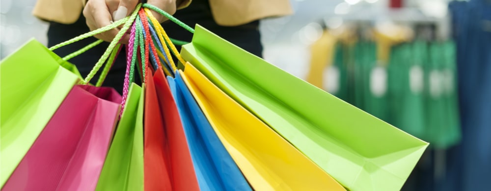 Person holding multiple colorful shopping bags in bright green, pink, red, blue, and yellow.