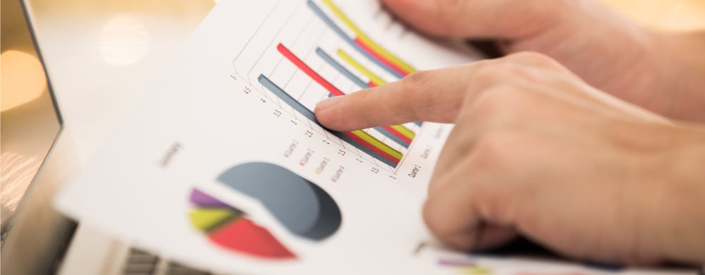 Person pointing at a printed bar chart and pie chart on a document.
