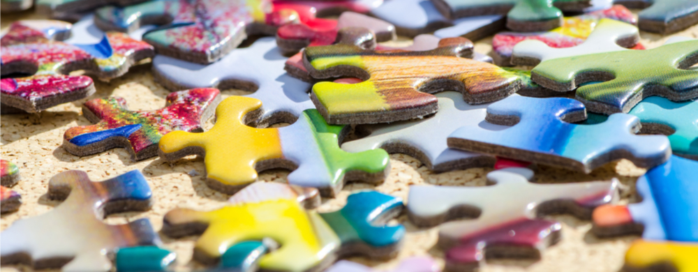 Colorful jigsaw puzzle pieces scattered on a sandy surface.