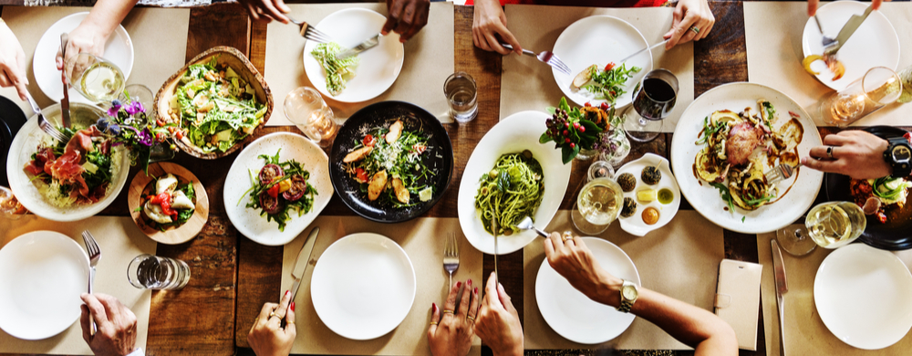 Overhead view of a wooden table with multiple diners sharing various salads and dishes.